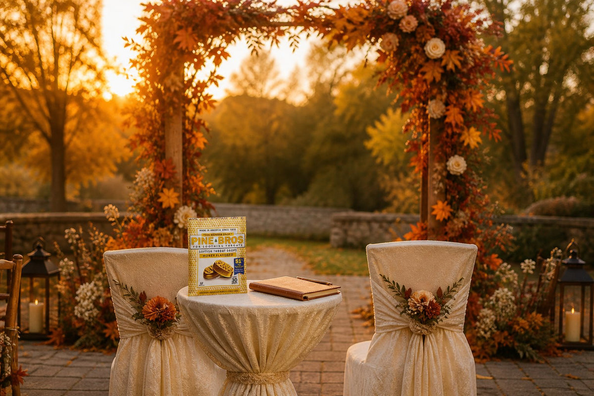 A small archway with autumn leaves in a garden, a podium with a notebook and a Pine Brothers Honey pouch resting beside it, two ceremony chairs draped with a cream cover, golden October light