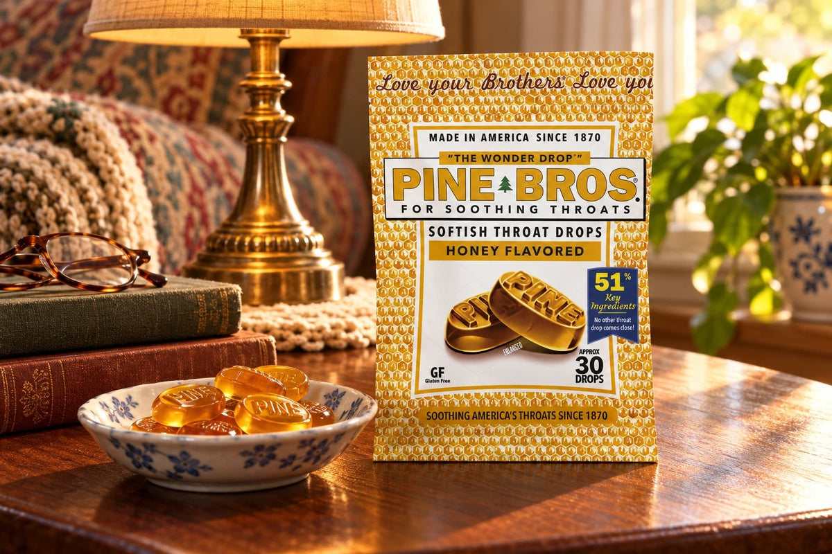 A Pine Brothers Honey pouch on a side table beside a reading lamp, folded glasses, old books and a dish of amber drops