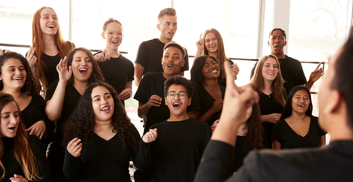 A student choir in black shirts singing together while their director leads them