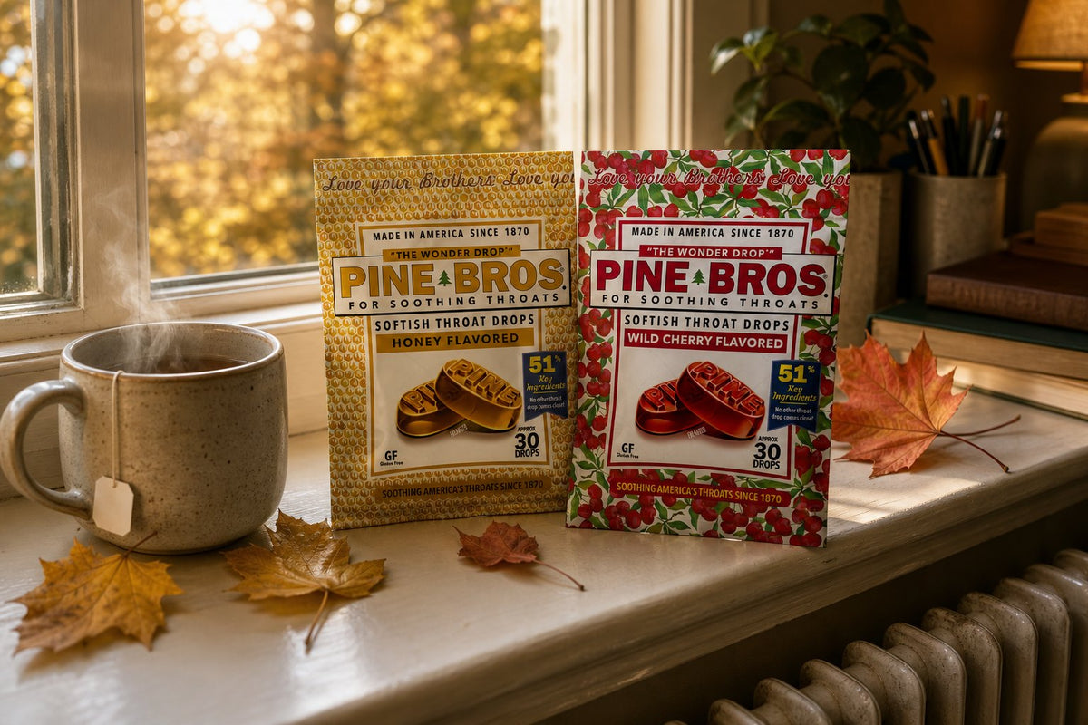A warm office windowsill in early October with a radiator below, a mug of tea, and Pine Brothers Real Honey and Wild Cherry packs, golden afternoon light