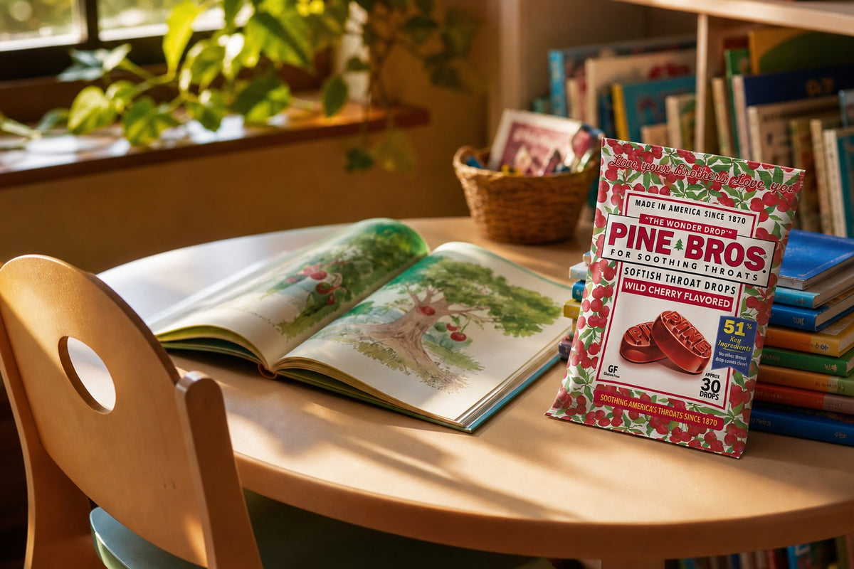 A cozy reading corner with an open picture book on a table, a child-sized chair, and a Pine Brothers Wild Cherry pack beside a stack of library books, warm afternoon light