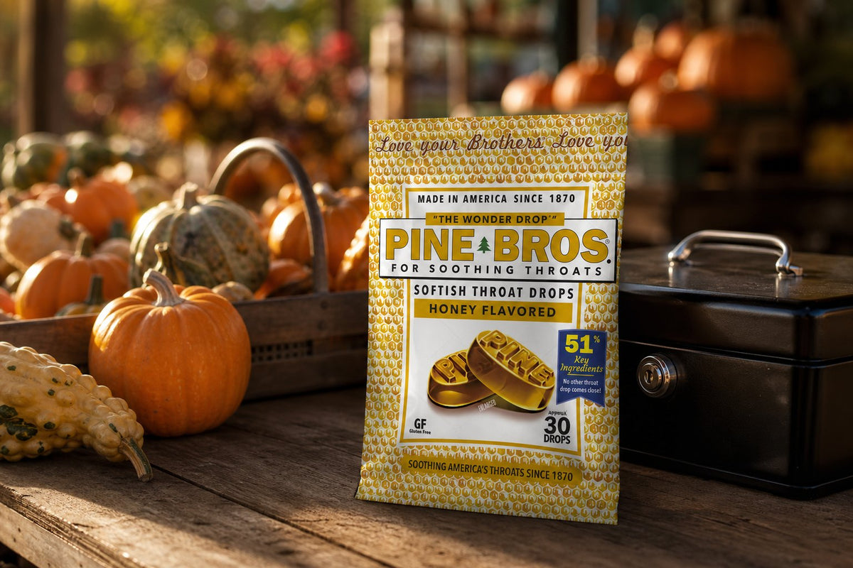 A farm stand counter at a pumpkin patch in October, pumpkins and gourds stacked, a Pine Brothers Real Honey pack beside the cash box, warm afternoon light
