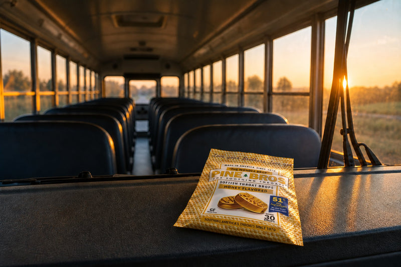 A school bus interior at dawn, seats in a row, morning light through the windows, and a Pine Brothers Honey pouch on the dashboard ledge, quiet early light