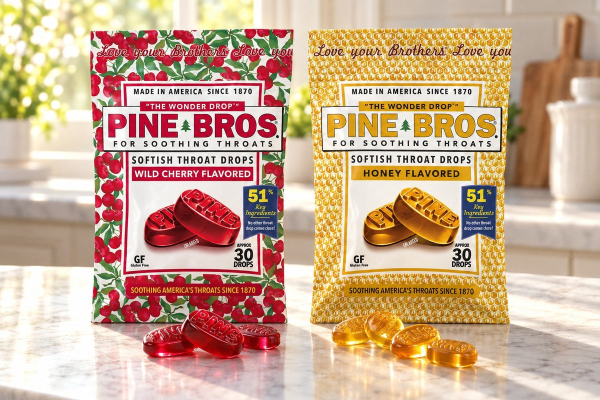 Pine Brothers Wild Cherry and Honey softish throat drop pouches side by side on a sunny kitchen counter, with red and amber drops in front