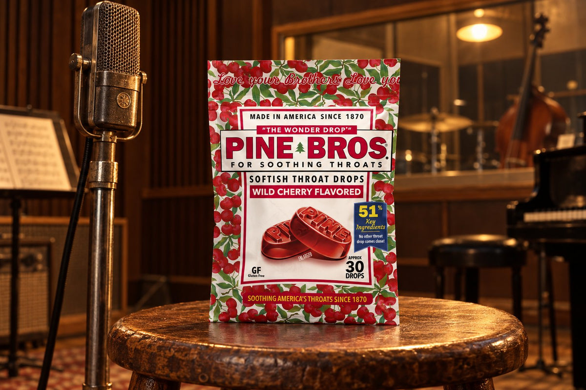 A Pine Brothers Wild Cherry pouch on a wooden stool beside a vintage studio microphone in a warmly lit recording room